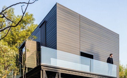 La casa de fachada oscura, con una persona en la terraza