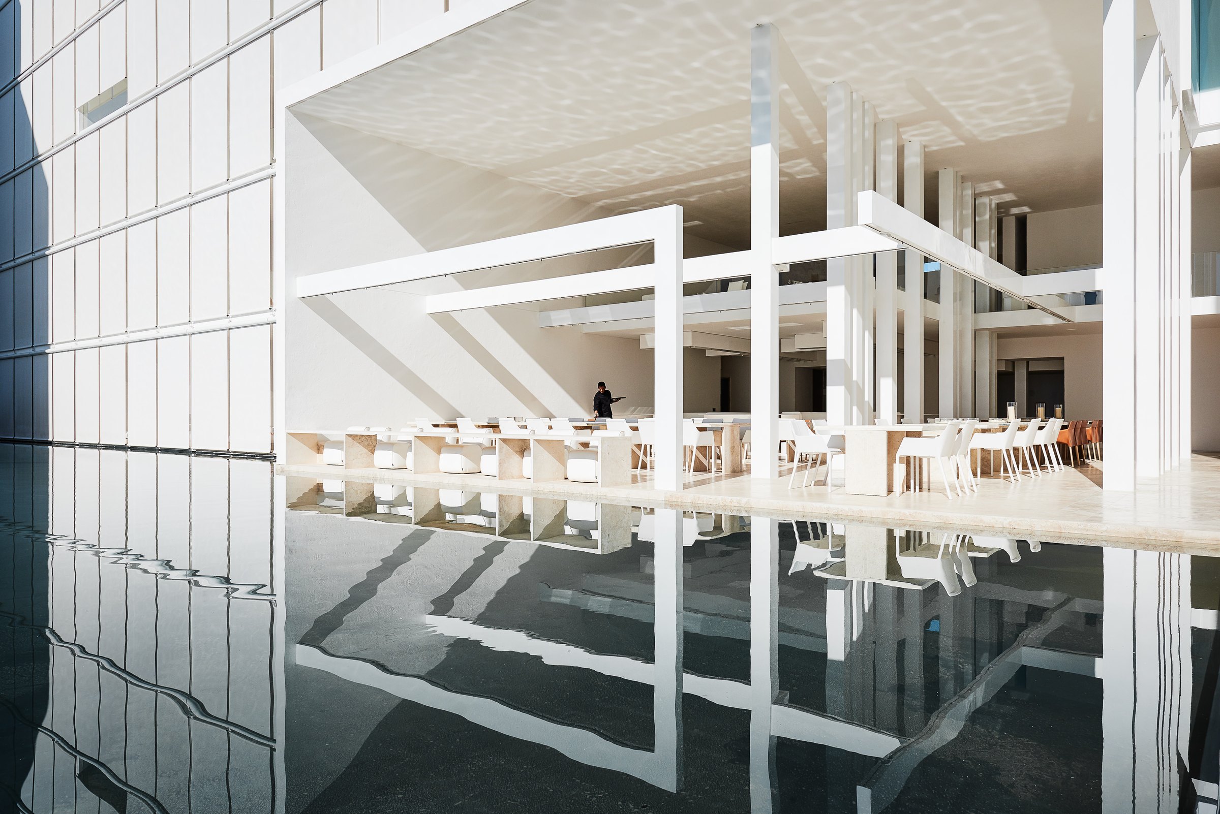 El comedor bajo la pérgola blanca, reflejado en el agua